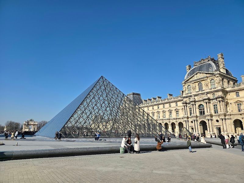 The glass pyramid of the Louvre Museum in Paris with visitors in the courtyard